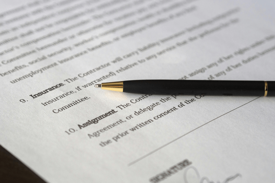Close-up of a legal contract with a black pen resting on sections for insurance and assignment, symbolizing contract law and legal agreements.
