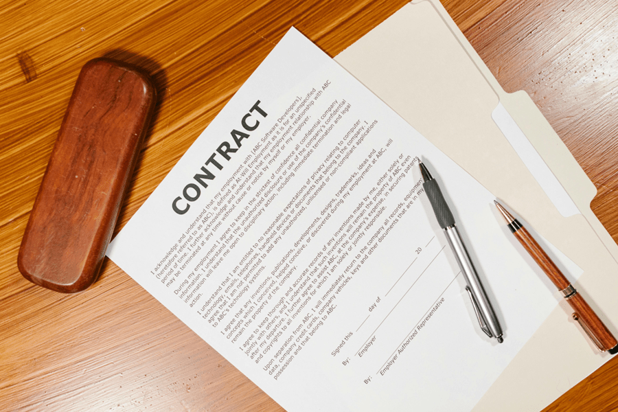 Top view of an employment contract on a wooden desk with two pens and a wooden case, representing labor law and hiring agreements.