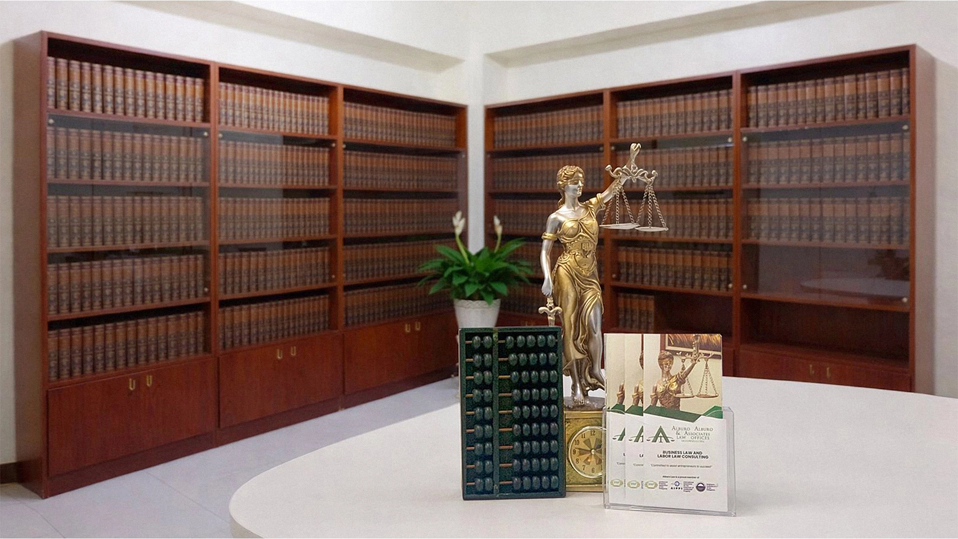 Lady Justice statue and abacus on a desk in the Alburo Law Office library, featuring shelves of SCRA (Supreme Court Reports Annotated) law books.
