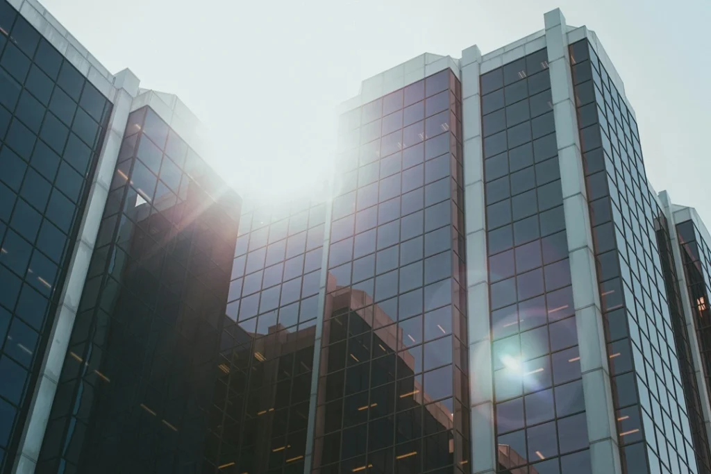 Low-angle photography of a modern glass skyscraper reflecting a clear blue sky